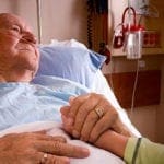 Old man lying in hospital bed holding daugher's hand