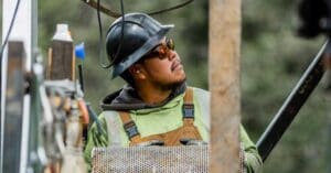 Construction worker in a hard hat and safety vest looks up at something off-camera on a construction site.